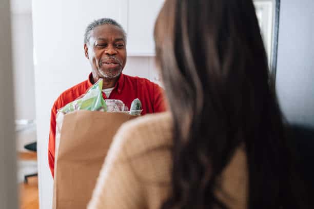 A young female Errand girl brings bag with food to an older man's front door