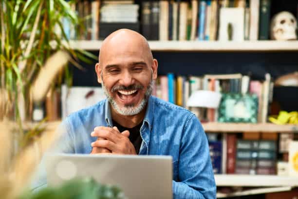 Cheerful handsome data entry worker at home speaking on video call using laptop, happiness, carefree, relaxation, communication