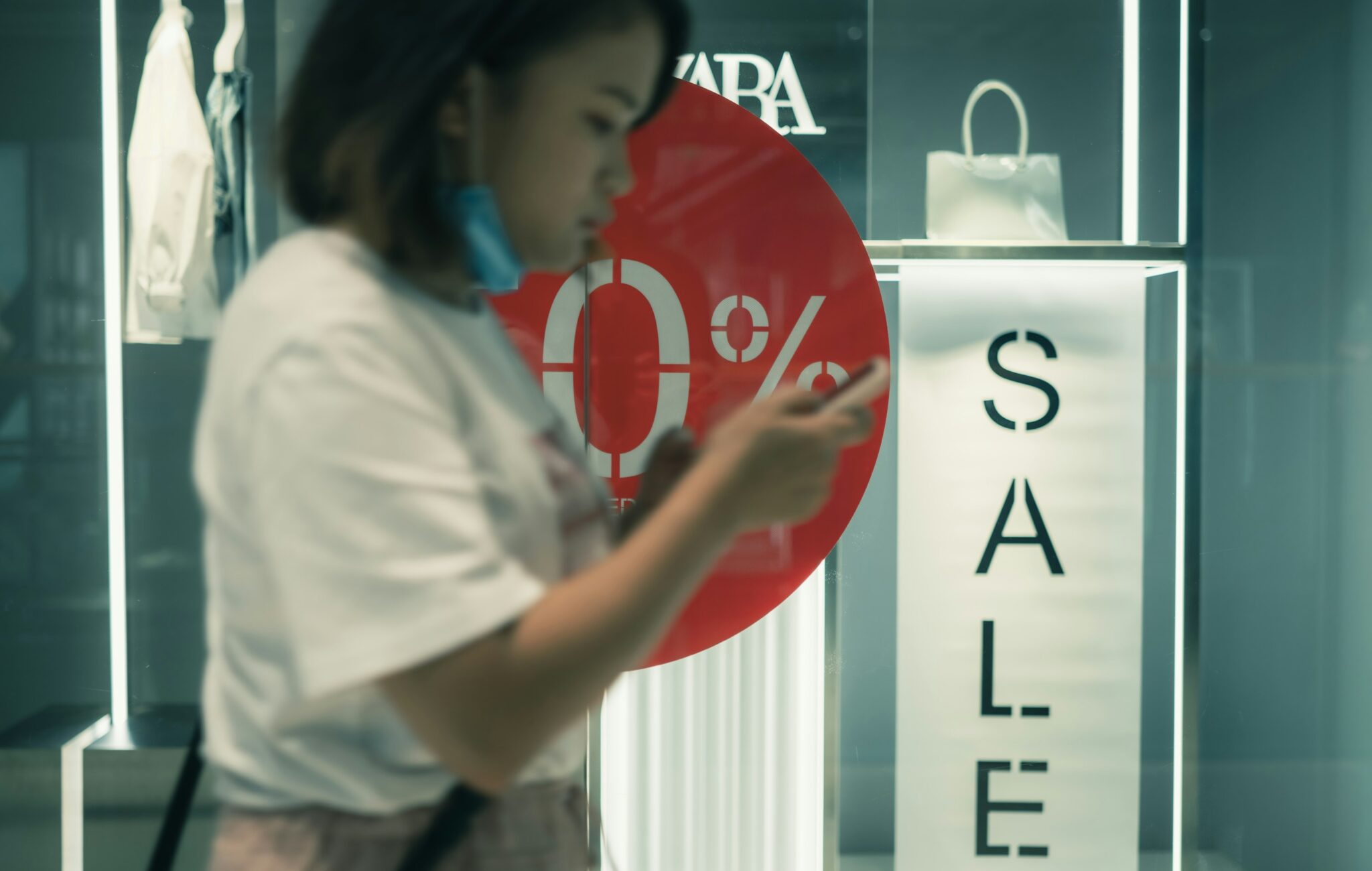 A lady tracking sells using her phone with sale written on the background.