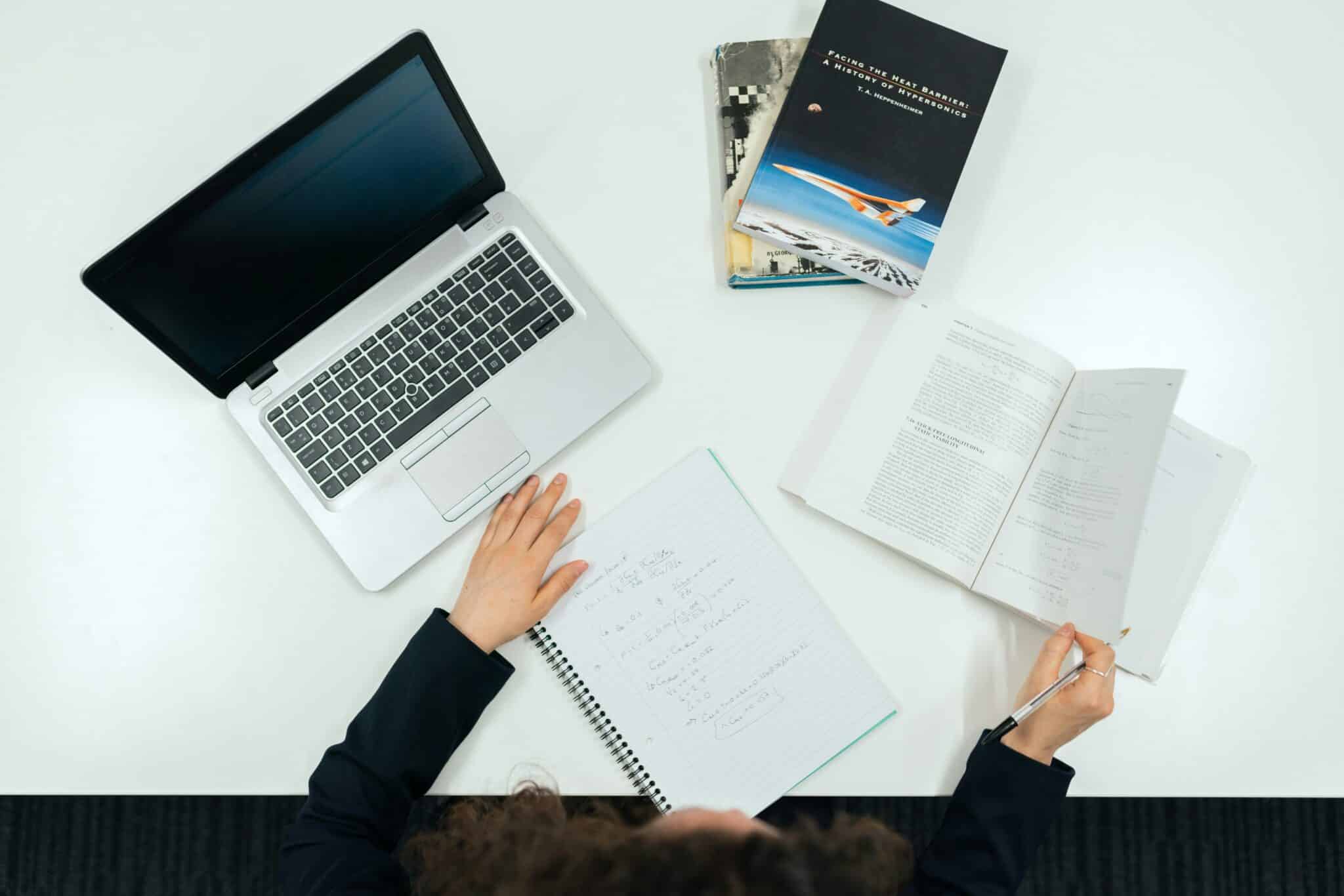 Man hands on table with a note, laptop and pen.